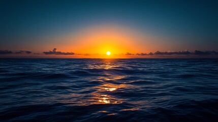 Obraz premium The sun sinks below the horizon, casting an amber glow on the ocean's surface. The sky above is a deep, inky blue.