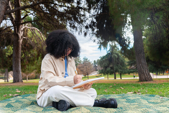 Young black artist sketching in a serene park surrounded by trees
