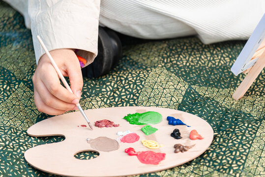 Young artist preparing palette with paints on patterned blanket