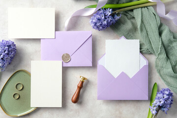 Elegant wedding invitation set with blank cards, purple envelopes, wax seal, and gold rings on a green dish, surrounded by hyacinth flowers and green fabric. Perfect for wedding stationery mockups