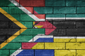 colourful painted big flag of south africa and flag of mozambique on a massive old brick wall...