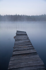 Obraz premium An old, wooden jetty in a calm lake in the forests of Finland on a foggy spring morning