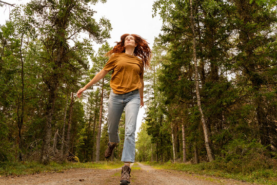 Young woman running freely in scenic Swedish forest trail
