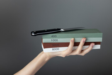 on a dark gray background in a woman's hand there are sharpening stones of different colors and abrasiveness, gradation of hardness, small steel knife on top of the stones