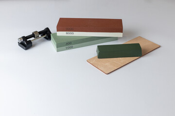 white background on table lies all the equipment a set for sharpening polishing kitchen knives and various blades different abrasiveness of stones a retainer for knives sheet tanned leather goya pasta