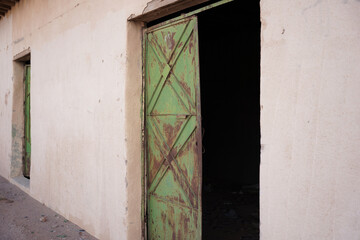 An old Saudi building with a weathered green metal door partially open, revealing a dark interior....