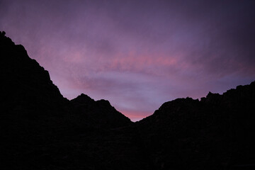 A dramatic silhouette of Saudi mountains at sunset, with a sky painted in pink and purple hues. A serene and atmospheric scene capturing the natural beauty of the Arabian landscape at dusk.