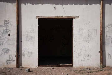 An abandoned building in the Saudi desert with a dark doorway and faded graffiti on weathered...
