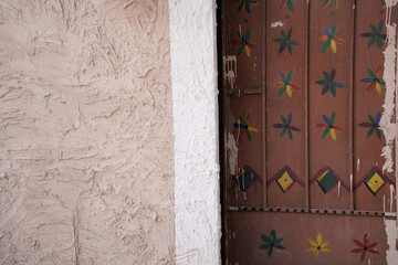 Close-up of a traditional wooden door decorated with colorful geometric and floral patterns, set beside a textured beige wall. A rustic detail reflecting cultural heritage and handcrafted design.