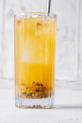 Passion Fruit Caipirinha cocktail in highball glass with straw on white wooden