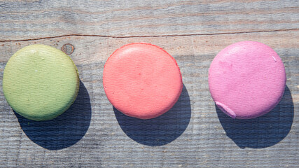 Three different colored macarons are sitting on a wooden table