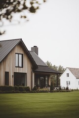 Obraz premium A contemporary wooden house stands gracefully next to a charming traditional white home, both nestled in a tranquil green landscape under a cloudy sky