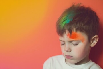 Naklejka premium Young boy with colorful face paint against a vibrant orange background, expressing a thoughtful emotion, ideal for themes of creativity, childhood, and playfulness