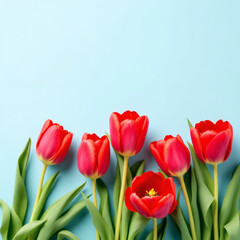Fototapeta premium Beautiful red tulips with green leaves on a light blue table. Pastel tones, closeup, congratulation theme. Perfect for text, quotes, or sayings. Top view with copyspace.