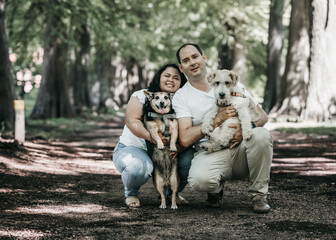 Portrait of a latin couple in a forest, they are with their dogs. One pet is a fox terrier wire and the other is black with beage