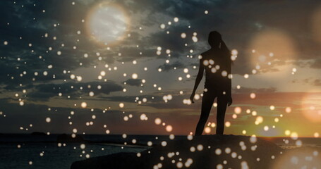 Silhouette of person dancing over glowing bokeh lights image at sunset
