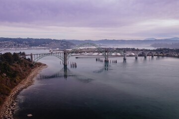 Fototapeta premium Coastal Yaquina Bay Bridge, at dawn, calm water reflects the structure. Cityscape and hills in the background. Peaceful morning scene. Oregon, USA