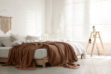 Large bed with blanket in mocha mousse shade indoors. Stylish bedroom interior with trendy color of 2025 year