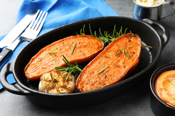 Halves of tasty cooked sweet potato with rosemary and garlic in baking dish served on grey table, closeup