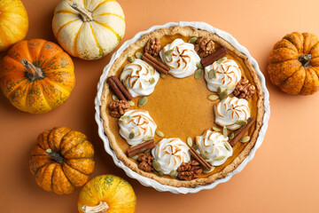 Delicious homemade pumpkin pie in baking dish and fresh pumpkins on orange table, flat lay