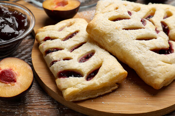 Delicious puff pastries, plums and jam on wooden table, closeup