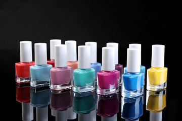 Set of different nail polishes in bottles on black mirror surface