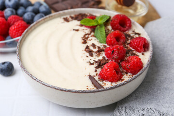 Tasty cooked semolina porridge with raspberries, chocolate and mint on white table, closeup