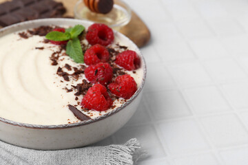 Tasty cooked semolina porridge with raspberries, chocolate and mint on white tiled table, closeup. Space for text