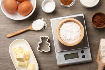 Kitchen scale with bowl of baking powder and other products on wooden table, flat lay