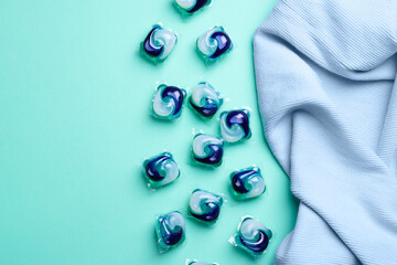 Laundry detergent capsules and clothes on turquoise background, flat lay