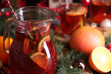 Tasty punch drink in glass jug and Christmas decor on table, closeup