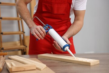 Worker with caulking gun glueing wooden plank indoors, closeup
