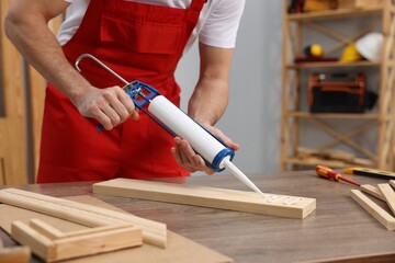 Worker with caulking gun glueing wooden plank indoors, closeup