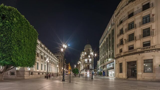 Avenida de la Constitucion night timelapse hyperlapse in Seville, Spain. Iconic Adriatica building glowing at evening. Historic architecture with modern streetlights, pedestrians and urban atmosphere