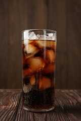 Cold cola with ice cubes in glass on wooden table, closeup