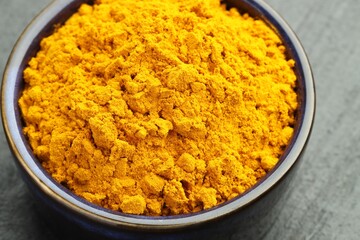 Turmeric powder in bowl on grey table, closeup