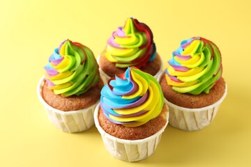 Tasty cupcakes with colorful cream on yellow background, closeup