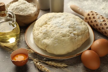 Fresh dough, ingredients and rolling pin on grey table, closeup