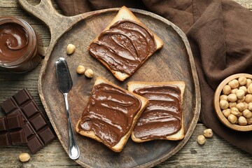 Tasty sandwiches with chocolate butter and hazelnuts on wooden table, flat lay