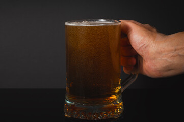 Mug of beer in a man's hand. Close up. Bubbles in the drink. Dark blurred background