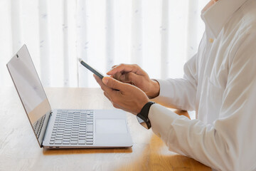 ノートパソコン前　スマホで作業をする男性の手元