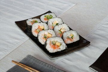 Homemade salmon salad sushi on black plate with white placemat on table. Japanese healthy food. Selective focus.