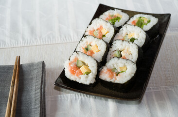 Homemade salmon salad sushi on black plate with white placemat on table. Japanese healthy food. Selective focus.
