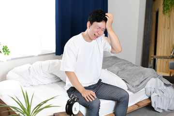 Fototapeta premium ベッドで頭痛に苦しむ若いアジア人の男性