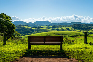 Fototapeta premium Serene Bench Overlooking Rolling Green Hills and Mountains under a Blue Sky
