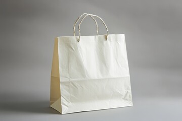 Cream paper shopping bag with twisted paper handles on gray background.