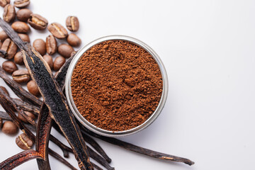 A cup of freshly brewed espresso sits beside aromatic vanilla pods and roasted coffee beans on a white background