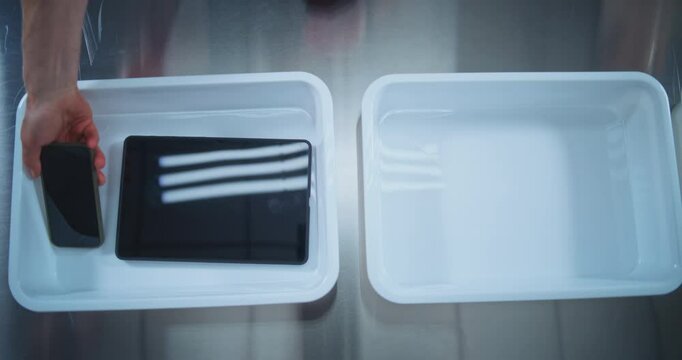 Top View on Passengers Placing Personal Items in Plastic Tray for Screening: Tablet Computer, Phone, Bag. Airport Security Checkpoint before Boarding Plane Flight. Security Officer Controls Procedure.