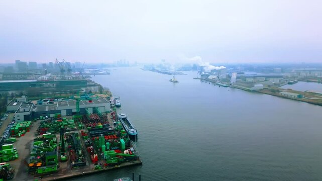Aerial shot of an industrial port in Amsterdam, showing cranes, factories, and ships docked along the river. The scene highlights trade, maritime industry, and large-scale logistics.