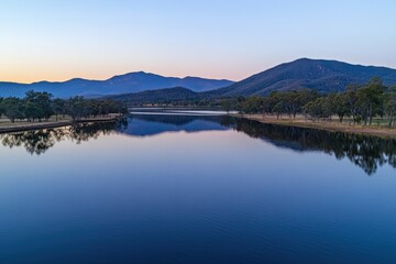 Serene Sunset Over Still Lake Surrounded by Majestic Mountains and Lush Green Trees in a Tranquil Natural Landscape